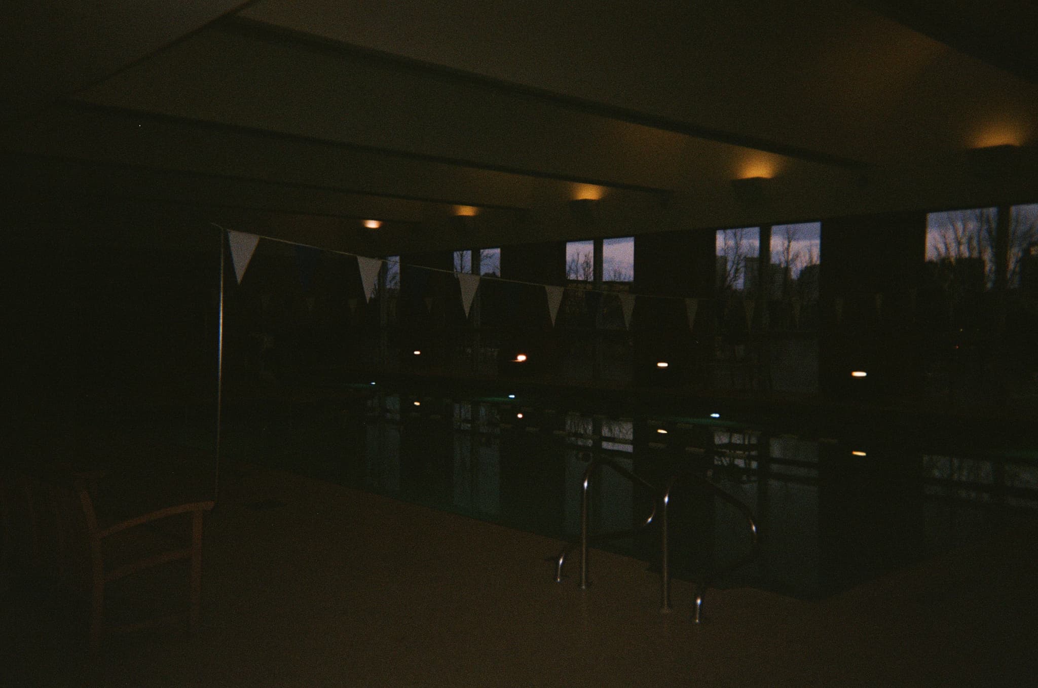 A dimly lit indoor swimming pool with lane dividers and windows along one side