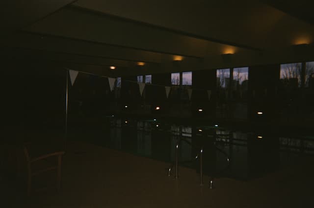 A dimly lit indoor swimming pool with lane dividers and windows along one side