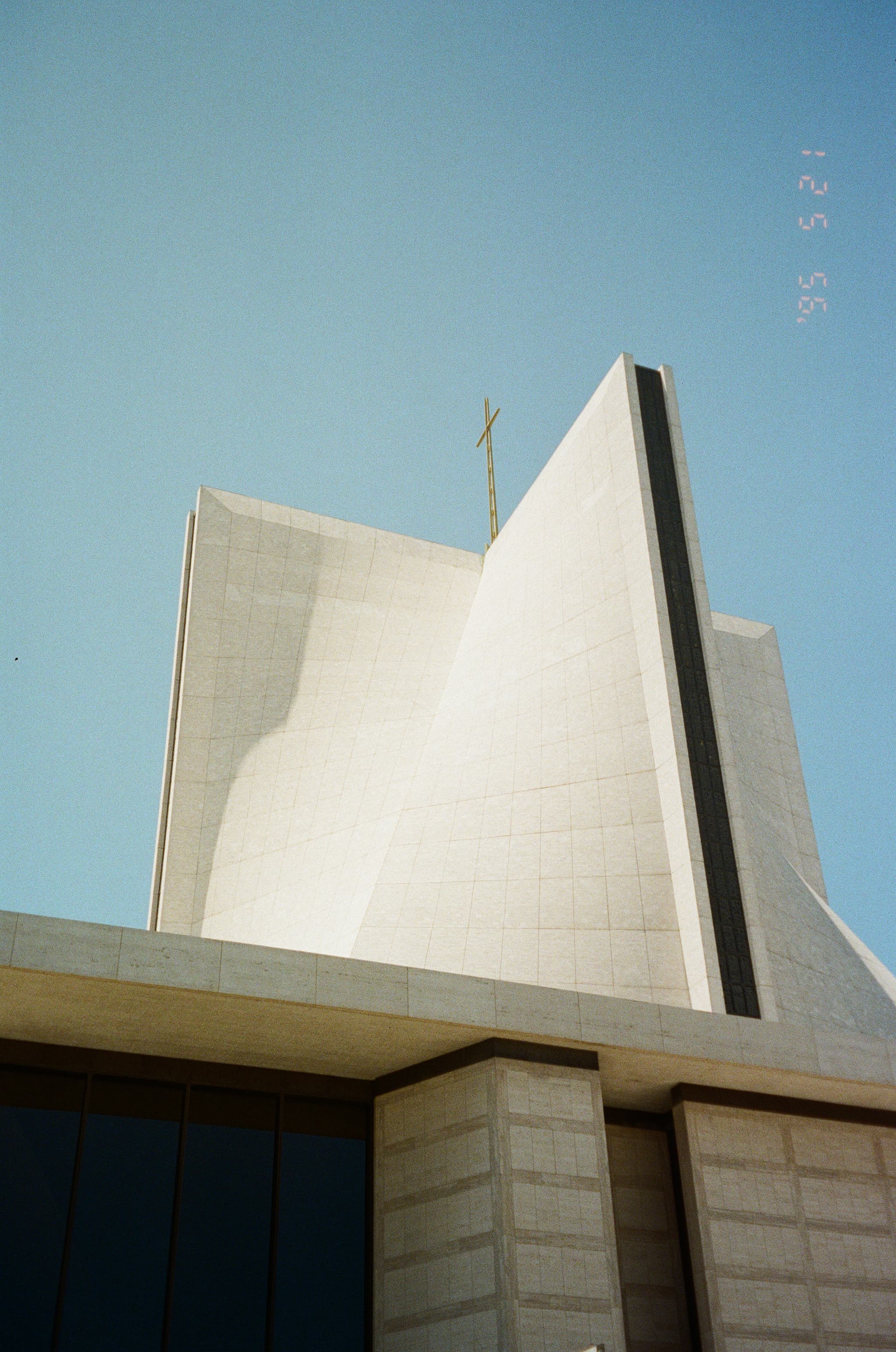 A modern church with a unique, angular design and a cross on top against a clear blue sky
