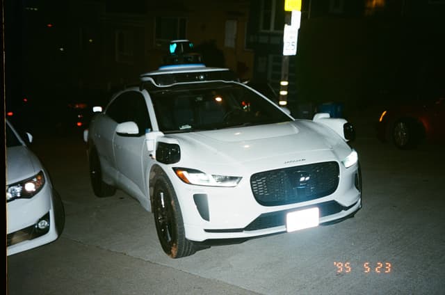 A white car equipped with sensors on the roof, parked on a street at night