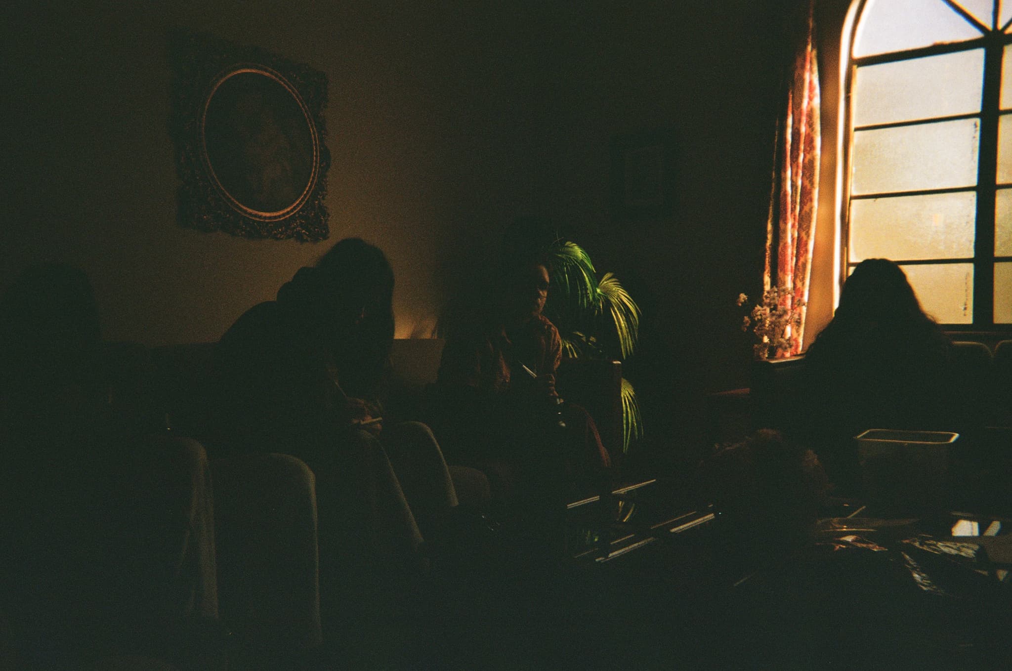 A dimly lit room with several people sitting, illuminated by light coming through a window