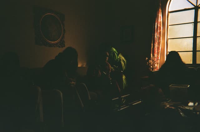A dimly lit room with several people sitting, illuminated by light coming through a window