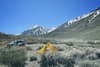 A yellow tent set up in a grassy area with a car parked nearby, surrounded by mountains under a clear blue sky
