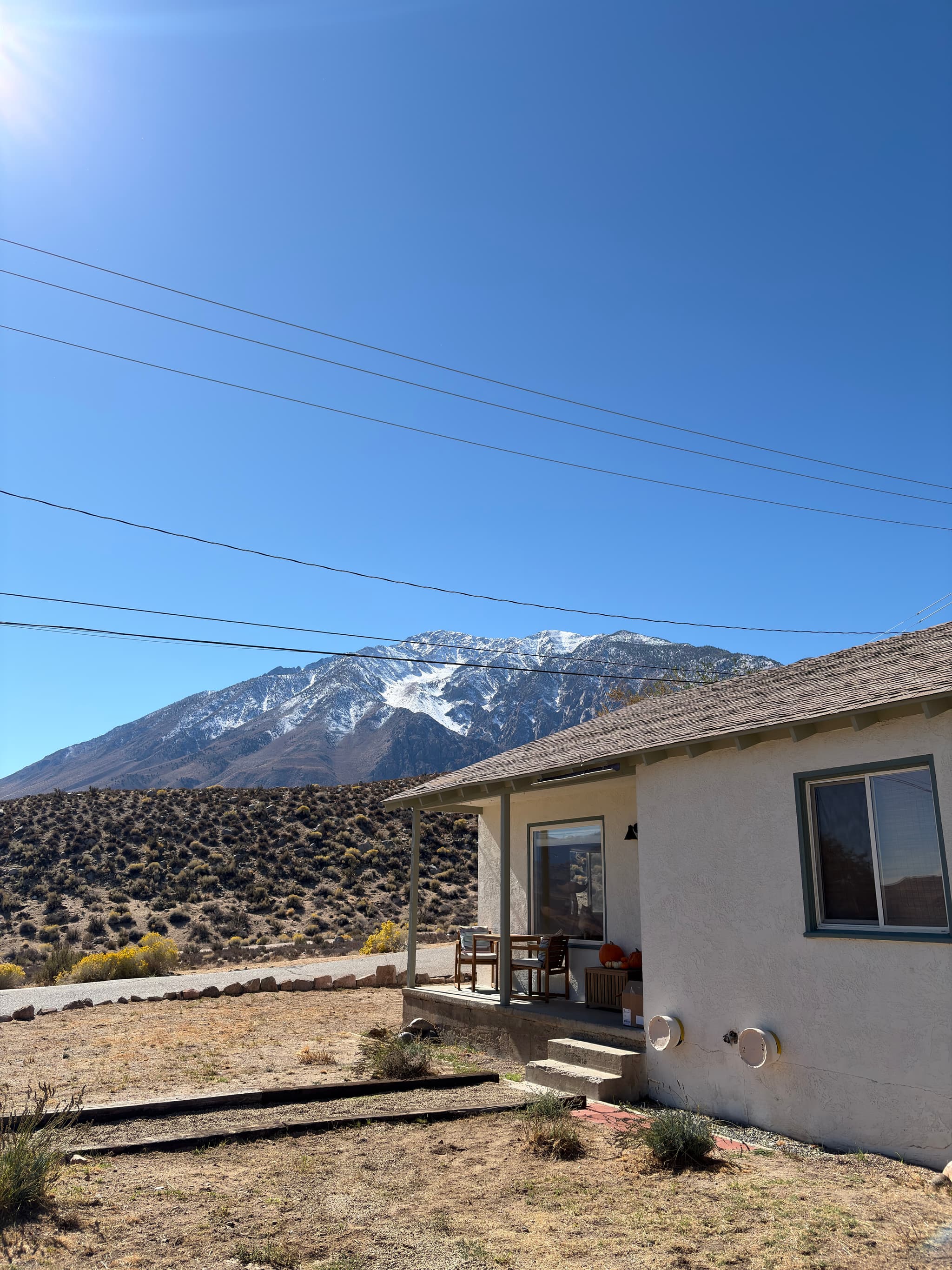 A small house sits in a dry, rocky landscape with a snow-capped mountain in the background under a clear blue sky