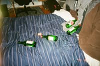 A bed with a blue striped blanket is scattered with several empty green bottles