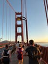 Runners crossing the Golden Gate Bridge at sunrise, with the red suspension towers and cables framing the roadway and bay in the background