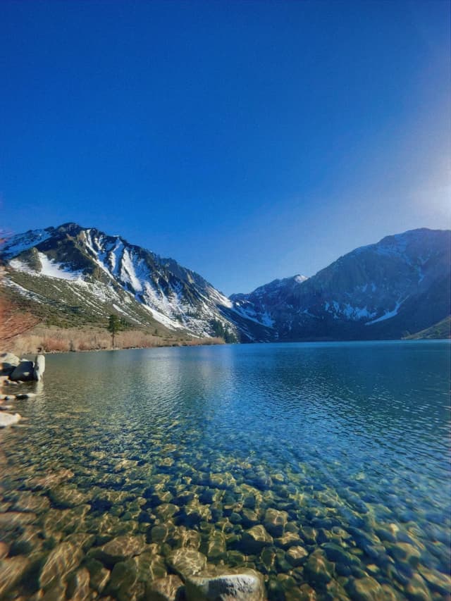A serene mountain lake with clear blue water, surrounded by snow-capped peaks under a bright blue sky