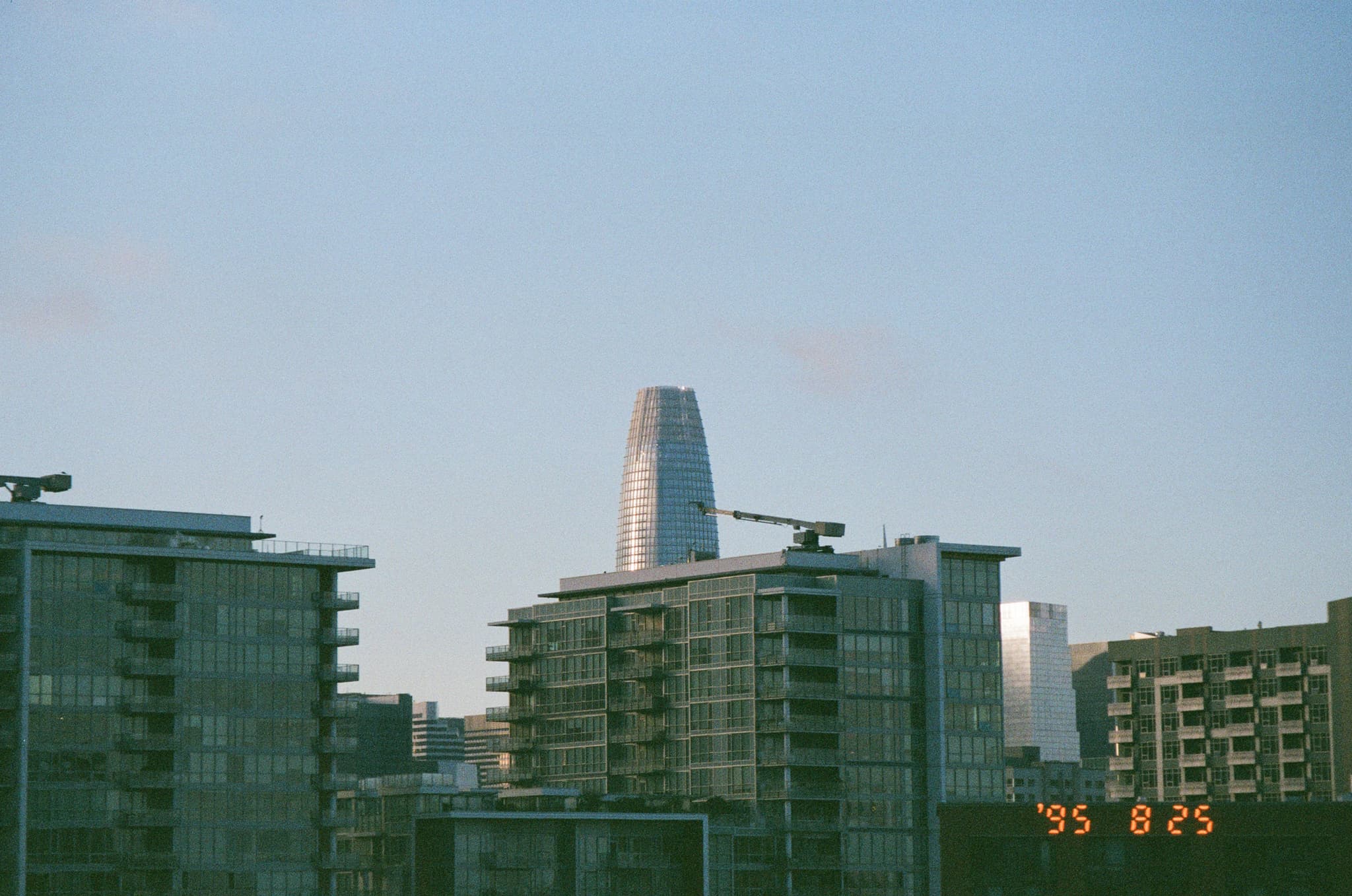 A modern cityscape with several tall buildings, dominated by a futuristic tower in the center under a clear blue sky