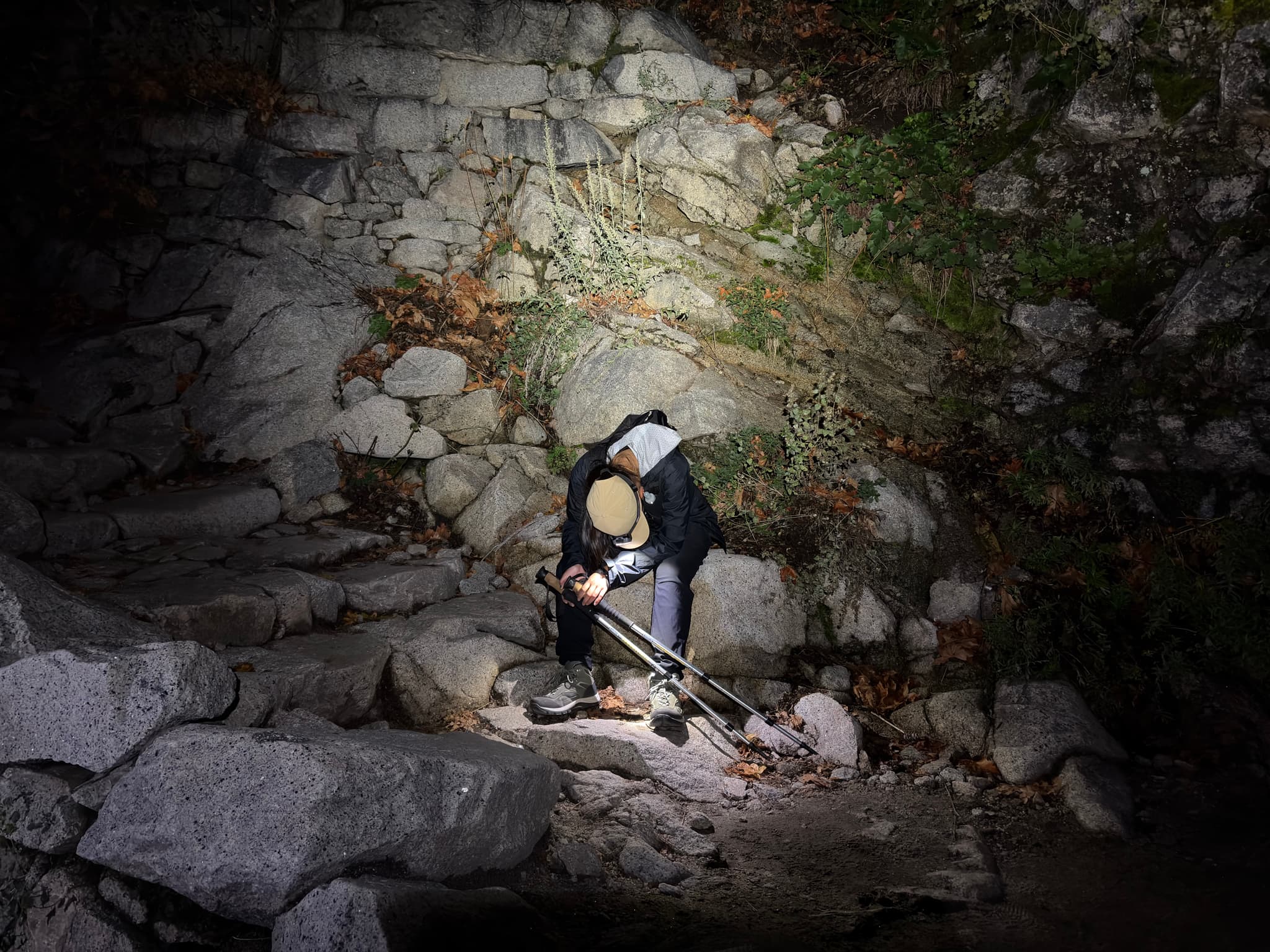Person using a flashlight while rock climbing at night, surrounded by a rocky terrain