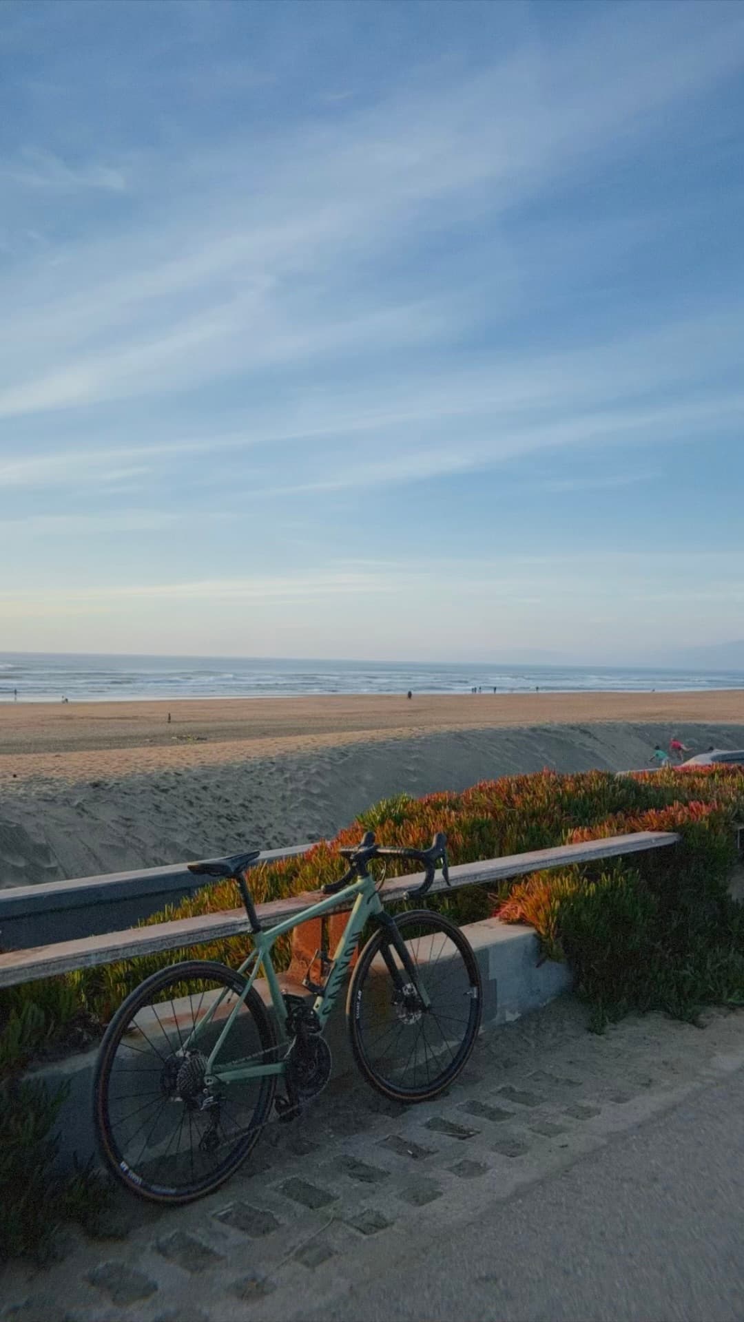 Road bicycle leaning against a seaside rail along a quiet sandy beach under a soft blue evening sky