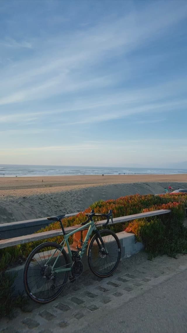 Road bicycle leaning against a seaside rail along a quiet sandy beach under a soft blue evening sky