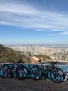 Panoramic cityscape viewed from a hilltop lookout with a graffiti-covered wall in the foreground under a blue sky