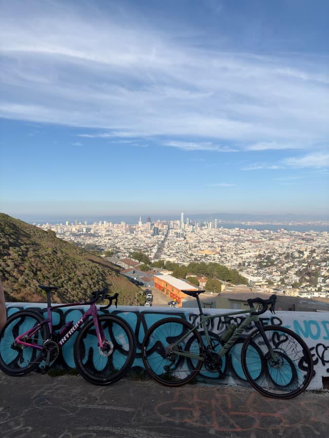 Panoramic cityscape viewed from a hilltop lookout with a graffiti-covered wall in the foreground under a blue sky