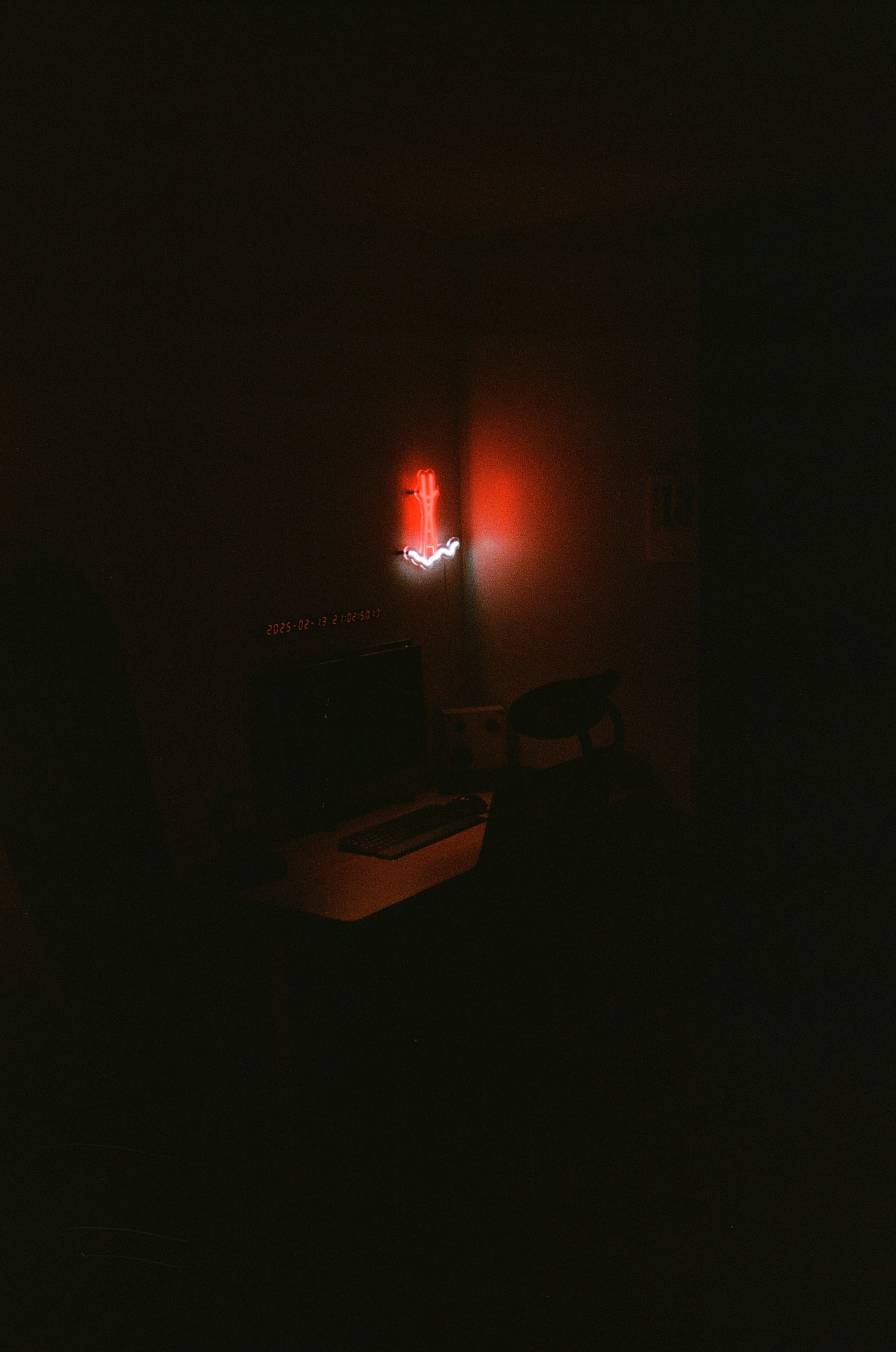 A dimly lit room with a desk and chair, illuminated by a red neon light on the wall