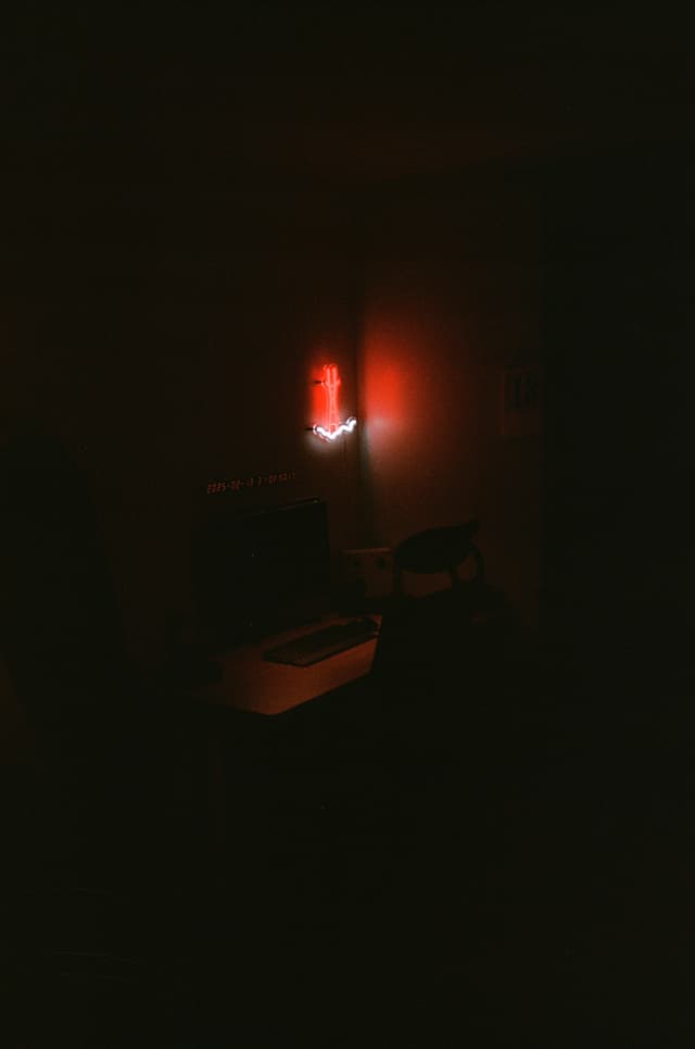 A dimly lit room with a desk and chair, illuminated by a red neon light on the wall