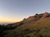 Golden-hour landscape of rolling green hills with a sunlit ridge under a pastel dusk sky, with distant haze on the horizon