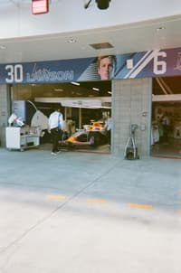 Formula 1 pit garage scene with mechanics around a race car, a large banner featuring the number 30 and Jacques Villeneuve, and equipment and tools set up in the pit lane