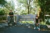 Two people are posing near a sign for the Visitor Center at a park, surrounded by trees and greenery